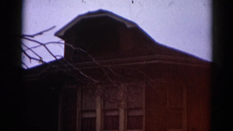 8mm film frame circa 1962 showing a brick residential house in Illinois; warm red cast and visible grain from aged emulsion.