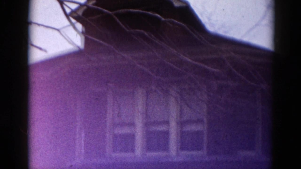 8mm film frame showing a brick house exterior dominated by a strong purple color aberration, consistent with dye-shift on aged 1960s reversal film stock.