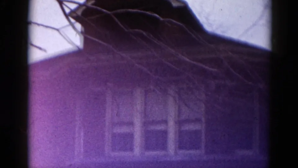 8mm film frame showing a brick house exterior dominated by a strong purple color aberration, consistent with dye-shift on aged 1960s reversal film stock.