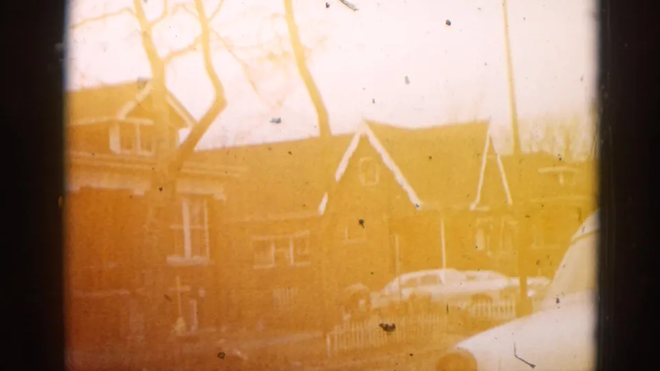 Brick residential building, bare trees, and a parked car viewed through heavy amber color drift in a 1962 Illinois 8mm home movie.