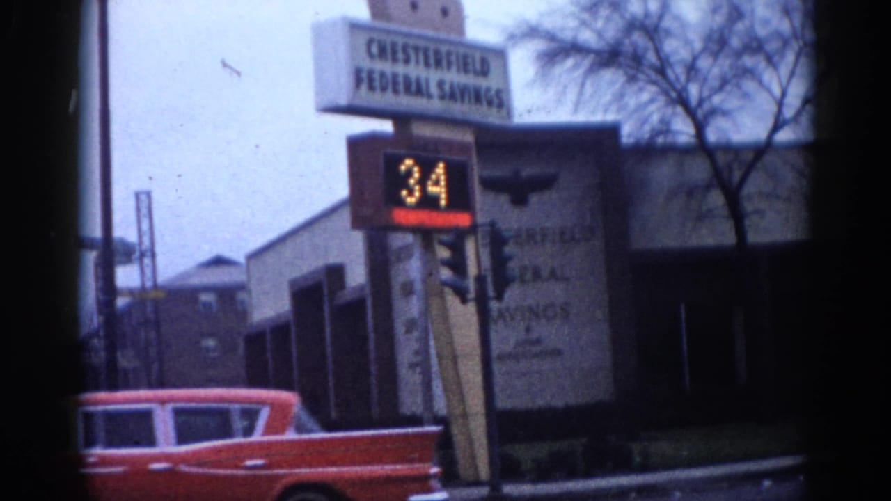 Street corner with Chesterfield Federal Savings bank sign, LED display showing 34, and a red classic American car at left, shot on 8mm film.