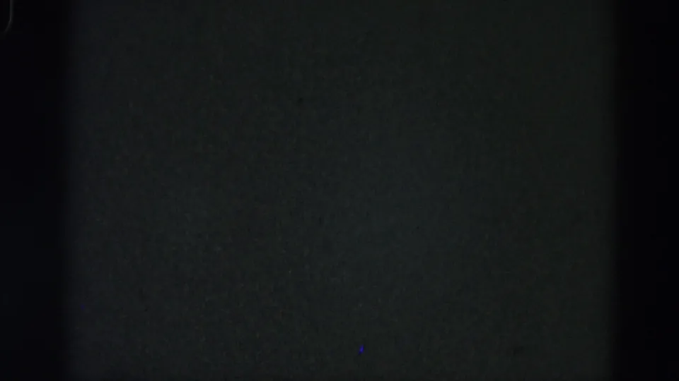 Damaged 8mm frame from a 1962 Illinois home-movie reel showing near-black field with faint blue artifact specks and coarse grain.