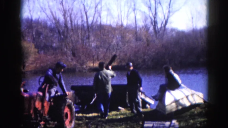 Three men in heavy work clothes beside a red tractor and large white structure on an Illinois riverbank, circa 1962.