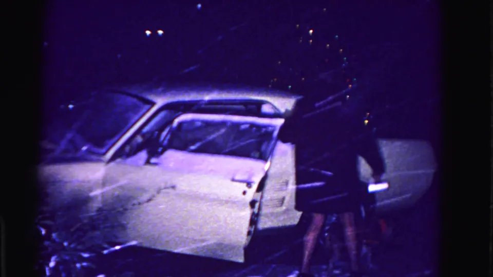 Woman stands beside the open door of a white early-1960s American sedan during heavy nighttime snowfall, Hagerstown, Maryland, 1962.