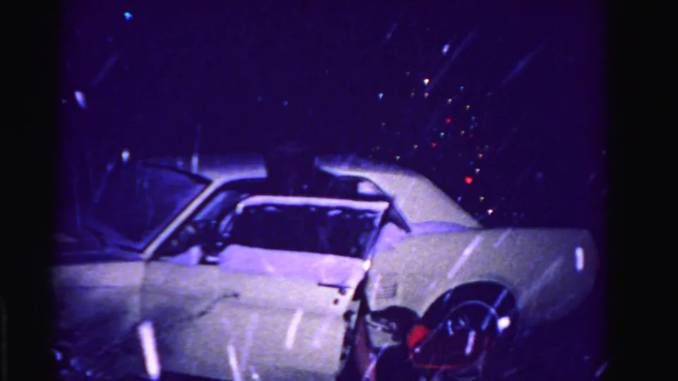 White early-1960s American sedan after woman has entered vehicle, colorful holiday-light bokeh overhead, wet pavement; Hagerstown, Maryland, circa 1962, 8mm.