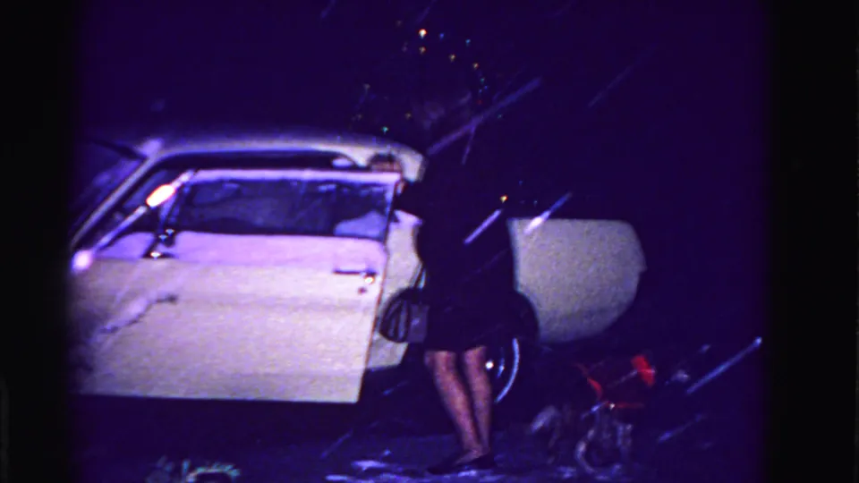 Woman in dark coat leaning into the open door of a white early-1960s car in heavy snow; dark handbag in hand, small red-coated dog at her feet, Hagerstown MD ca. 1962.