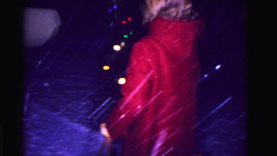 Woman in red coat walking outdoors at night in a snowstorm, colored holiday string lights in background, Hagerstown Maryland circa 1962.