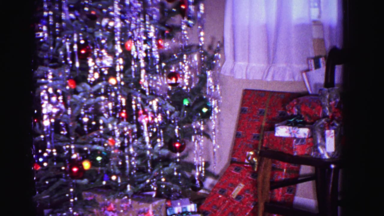 8mm home movie frame from 1962 showing a tinseled Christmas tree with colorful incandescent lights and gift-wrapped presents, Hagerstown, Maryland.