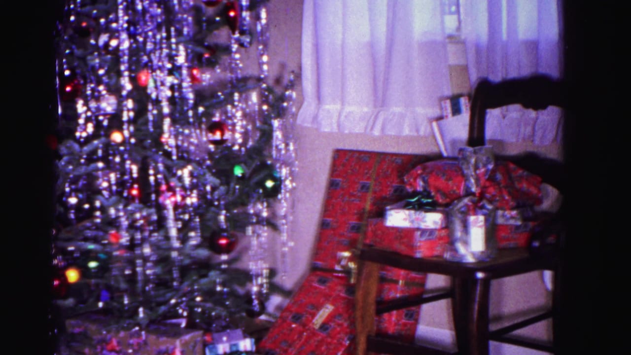 8mm footage from 1962 showing a tinseled Christmas tree, wrapped presents on a wooden chair, and a sheer curtain window treatment in a domestic interior, Hagerstown, Maryland.