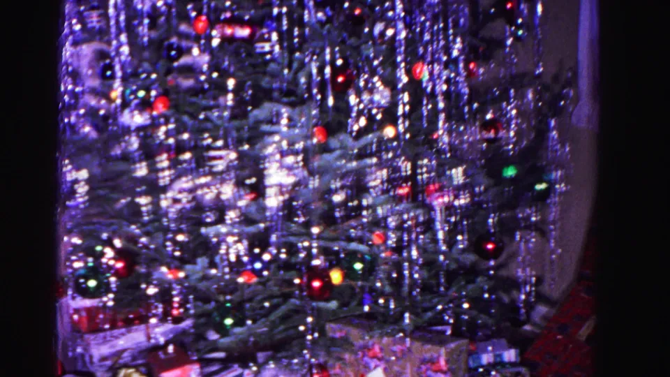 8mm home movie close view circa 1962: lower section of Christmas tree with heavy silver icicle tinsel and scattered red and green ornament lights.