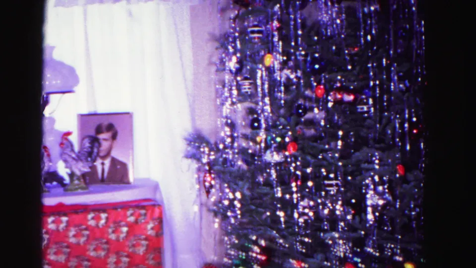 1962 home movie pan toward Christmas tree; silver tinsel, colorful ball ornaments, and string lights fill the frame with display table items receding into the background.