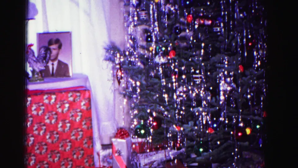 Final pan frame of 1962 Hagerstown Christmas scene; tinsel-laden tree with wrapped presents at its base and a framed portrait receding into the background.