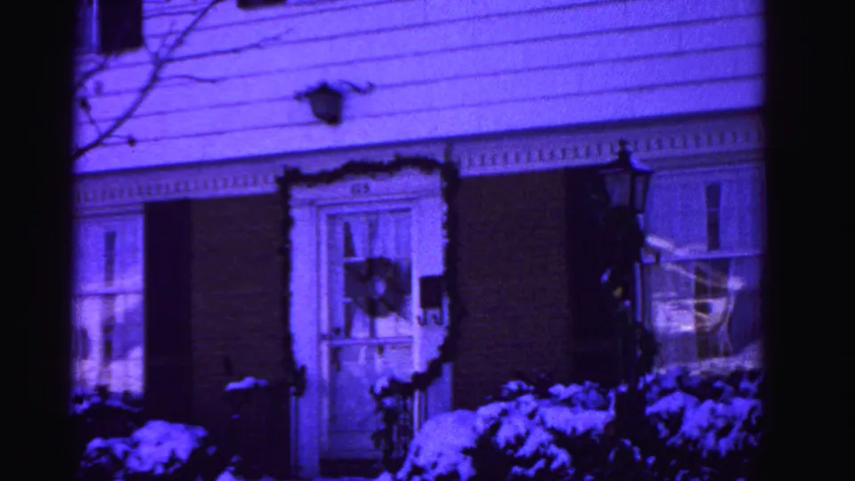 8mm home movie frame from 1962 showing a two-story Hagerstown, Maryland house with a Christmas wreath on the left window, snow-covered shrubs, and a strong purple film-aging color shift.