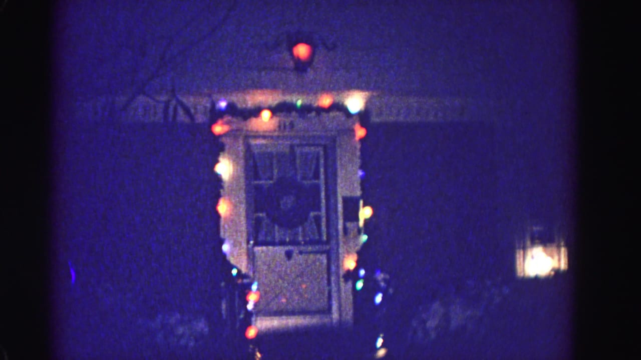 1962 home movie, front entrance strung with multicolored Christmas lights at night, porch or window light visible at right; Hagerstown, Maryland.