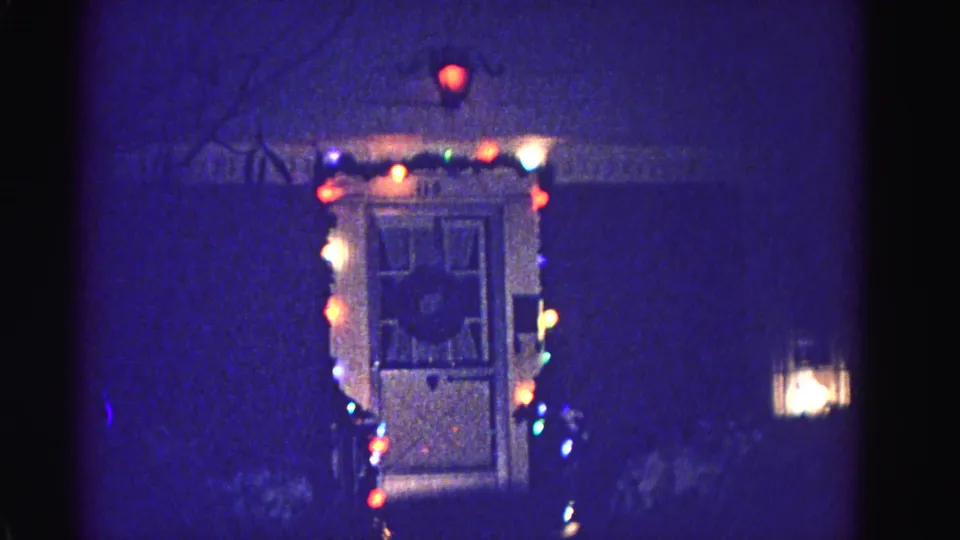 1962 home movie, front entrance strung with multicolored Christmas lights at night, porch or window light visible at right; Hagerstown, Maryland.