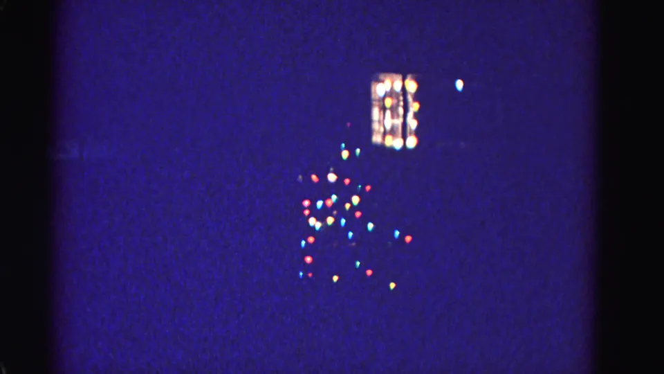 1962 home movie after slight pan, showing a lit window and a loose cluster of multicolored Christmas lights in the yard at night; Hagerstown, Maryland.