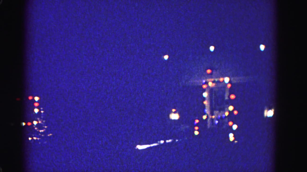 Blurred multicolored bokeh lights float against a deep blue night sky in 8mm footage.