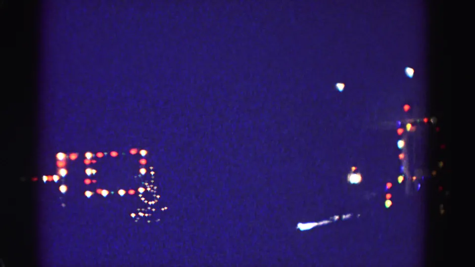 Multicolored holiday light bokeh in a deep blue night sky with a lamp silhouette at the right edge, 8mm home movie, Hagerstown Maryland, 1962.