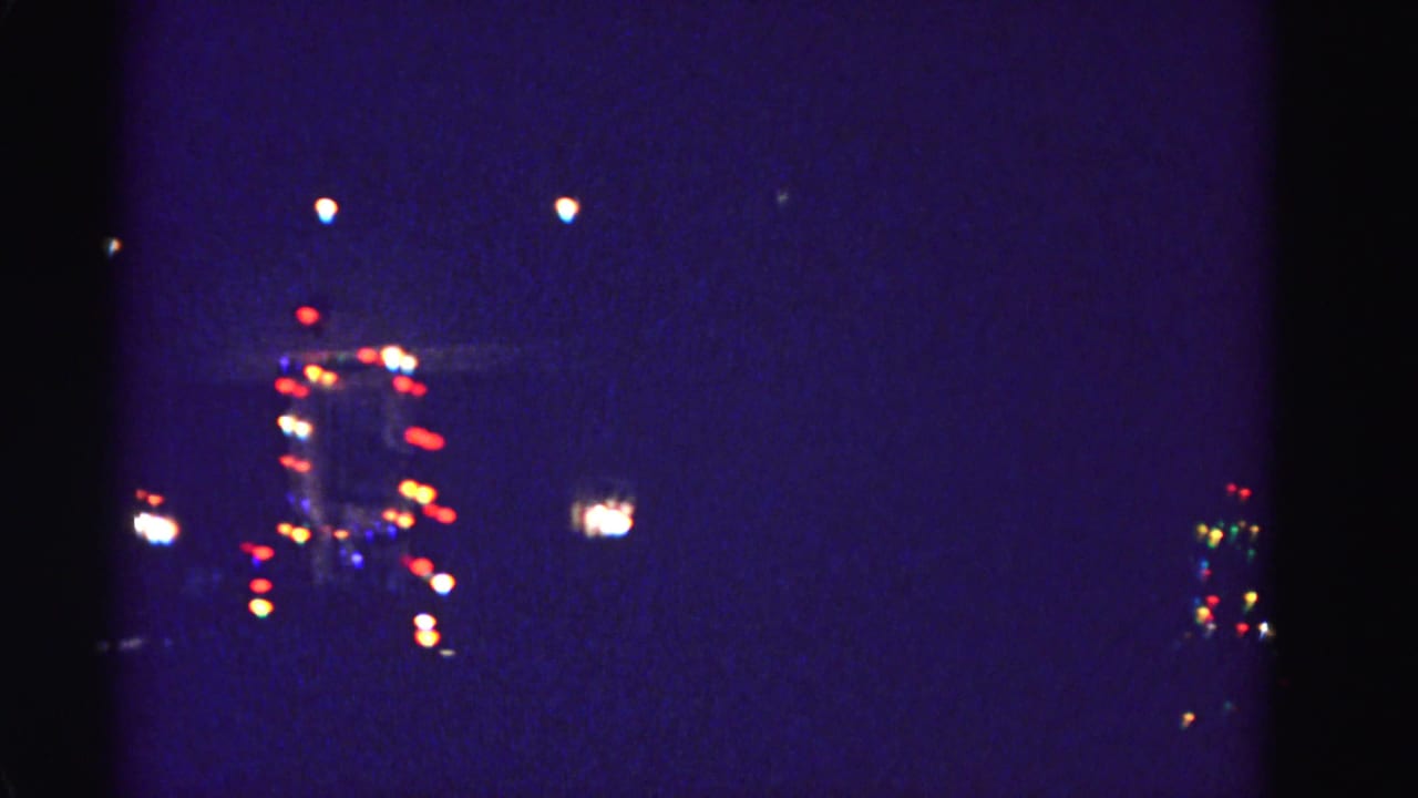 8mm home-movie frame circa 1962 of a distant festively lit building at night, attributed to Hagerstown, Maryland; heavy grain and vignette visible.