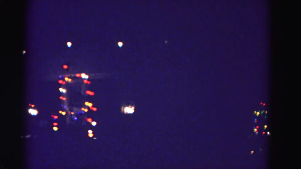 8mm home-movie frame circa 1962 of a distant festively lit building at night, attributed to Hagerstown, Maryland; heavy grain and vignette visible.