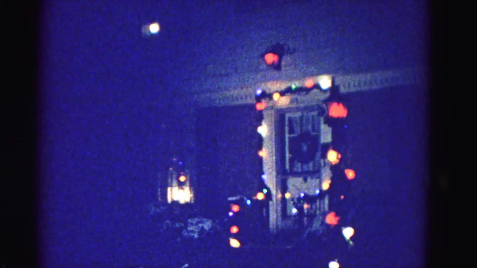 Final frame of a 1962 8mm home movie showing the same Christmas-lit residential house exterior in Hagerstown, Maryland with lantern fixture and window glow.