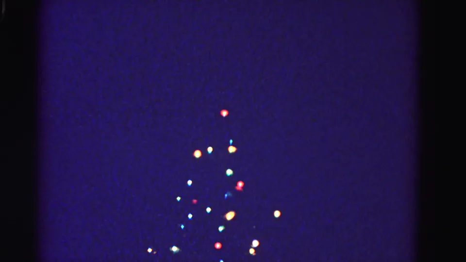 Outdoor Christmas tree decorated with multicolored lights against dark sky, circa 1962; strong blue-purple 8mm color shift and glowing light bloom throughout.