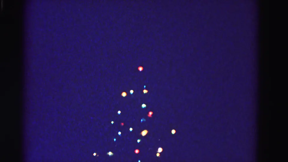 Outdoor Christmas tree with colorful string lights against dark night sky, circa 1962; blue-purple 8mm color cast is pronounced and lights bloom softly against darkness.