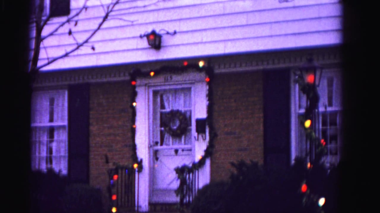 Suburban brick house in Hagerstown, Maryland, 1962 — front door with wreath and multicolored Christmas light garland, black shutters, and wall-mounted exterior lamp.