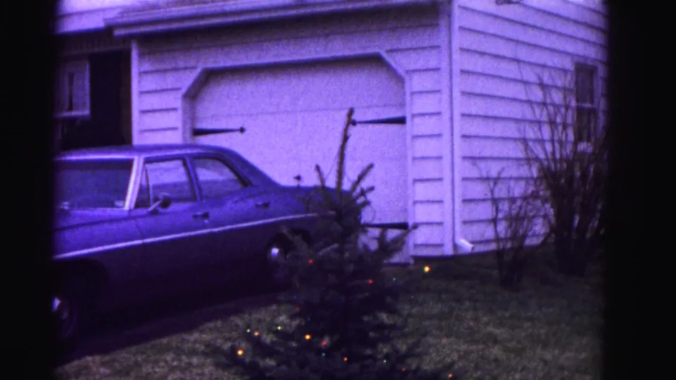 Suburban Hagerstown, Maryland driveway circa 1962 — white aluminum-sided garage, parked full-size American sedan, and small Christmas tree with colored lights in the yard.