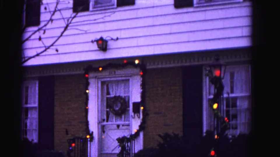 Wider 8mm frame circa 1962 showing the full front facade of a Hagerstown, Maryland house — bare winter tree branches, colored Christmas lights, and wall lantern visible.