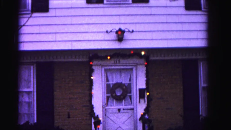 Residential front entry ca. 1962, Hagerstown, Maryland: door wreath, multicolored string lights along doorframe, and lavender color cast consistent with aged 8mm reversal film stock.
