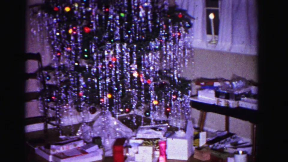 Final 8mm frame from 1962 Christmas home movie showing tinsel tree, gifts, a window candle, and a chair in a domestic interior, Hagerstown, Maryland