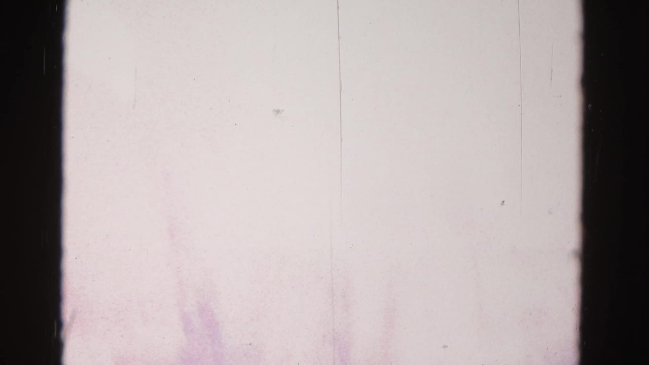 Near-white overexposed 8mm film frame, likely a reel splice or in-camera transition; faint silhouette visible at lower right corner.