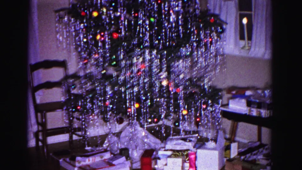 A heavily tinseled Christmas tree with multicolored incandescent bulbs and wrapped gifts at its base, shot in an apparent 1962 Hagerstown, Maryland living room on 8mm film.