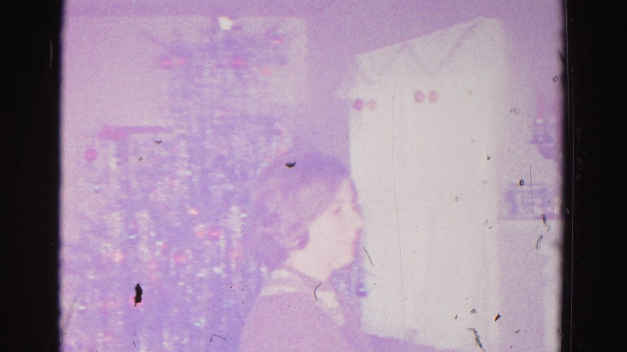 Closing frame of a 1962 8mm home movie showing a decorated Christmas tree with colored ornament lights, partially obscured by severe film deterioration, dye fading, and dark emulsion damage.