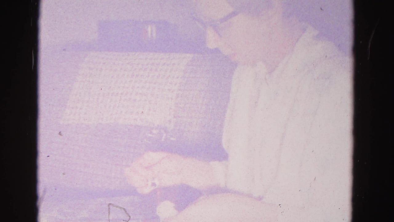 Overexposed 8mm frame with a partially visible figure beside a grid-textured couch; domestic interior, Hagerstown, Maryland, circa 1962.