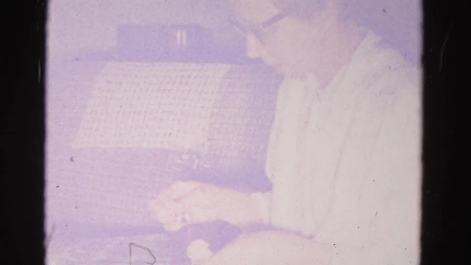 Overexposed 8mm frame with a partially visible figure beside a grid-textured couch; domestic interior, Hagerstown, Maryland, circa 1962.