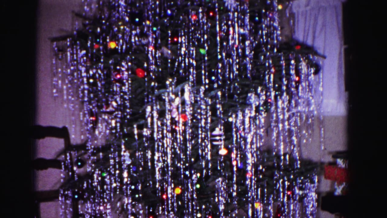 Christmas tree densely draped in silver tinsel with colorful ornaments; dark furniture form visible at right edge of frame.