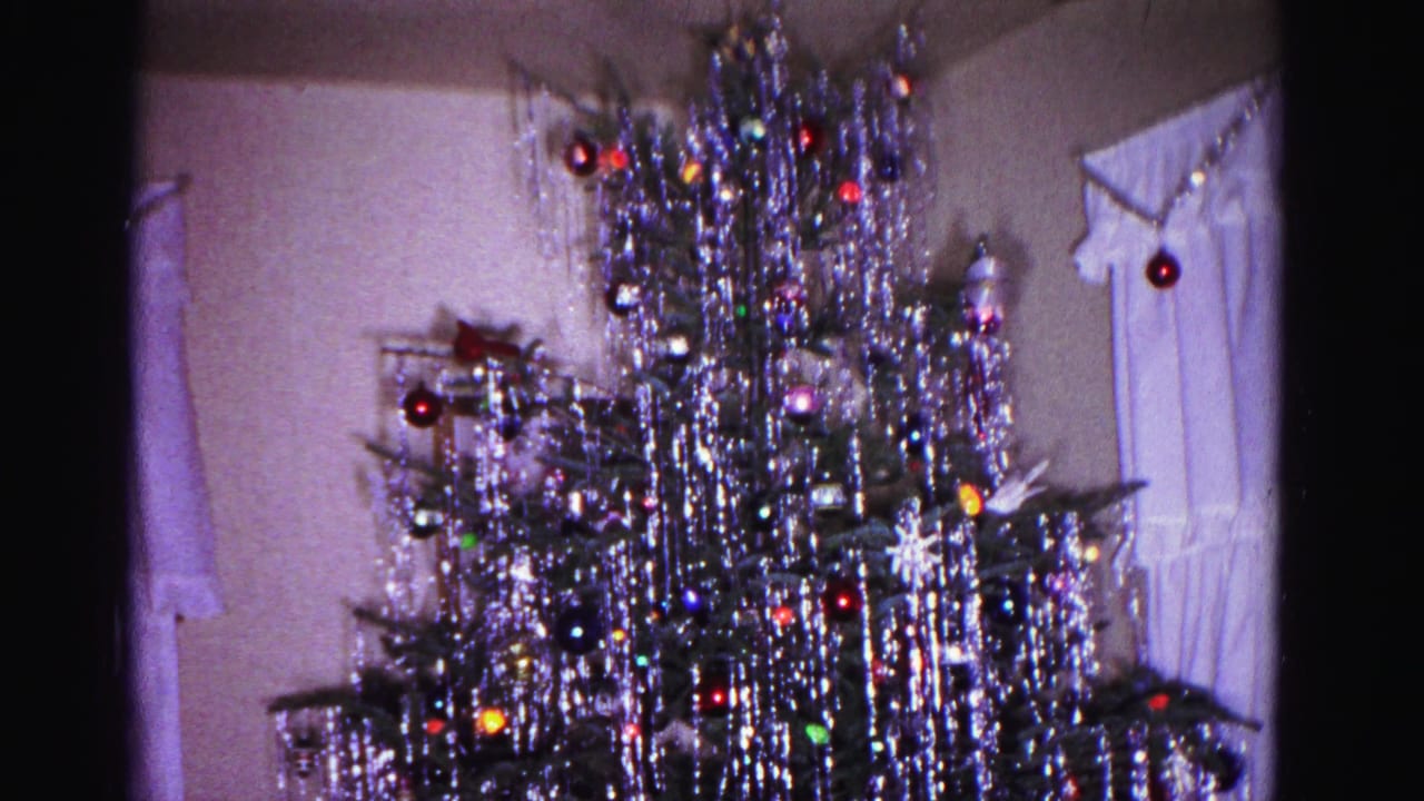 Tinsel-covered Christmas tree in a 1960s domestic interior; curtained window with possible candle or decorative item visible beside the tree, Hagerstown Maryland.