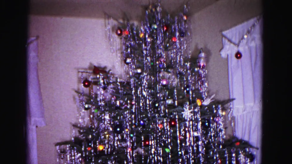 Tinsel-covered Christmas tree in a 1960s domestic interior; curtained window with possible candle or decorative item visible beside the tree, Hagerstown Maryland.