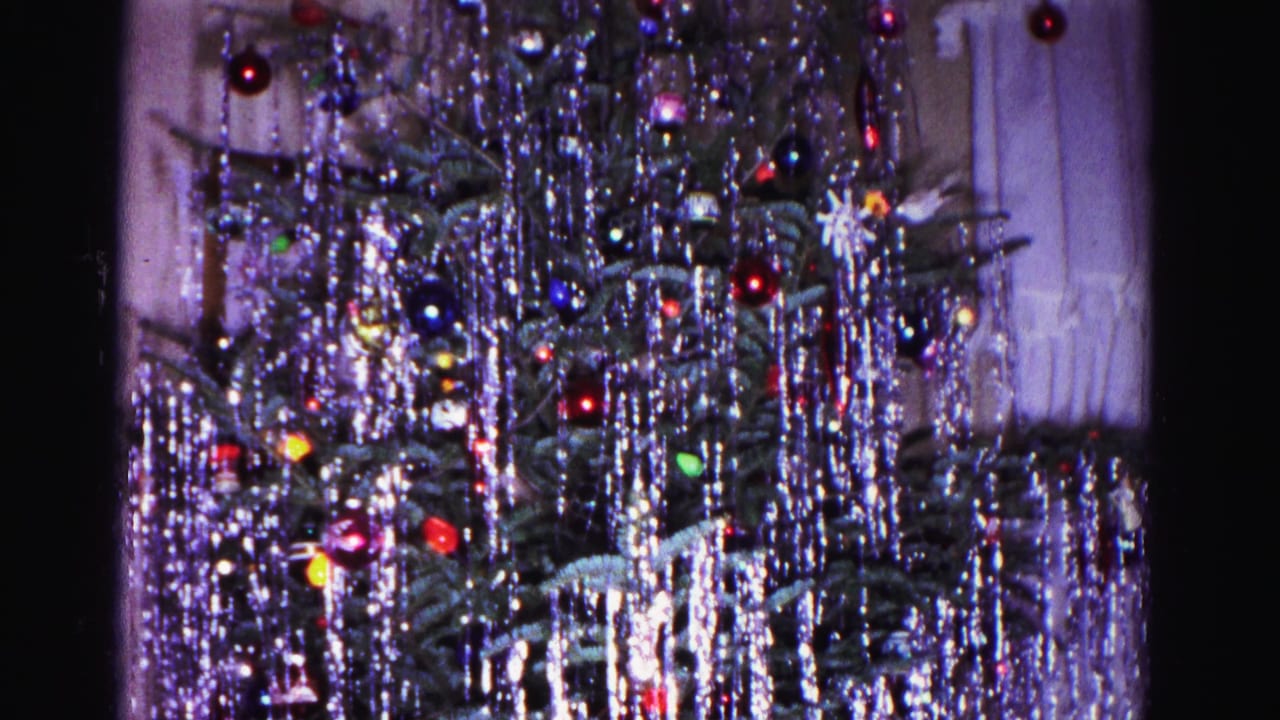 Close-up of a heavily tinsel-draped Christmas tree with colorful glass ball ornaments, filmed on 8mm.