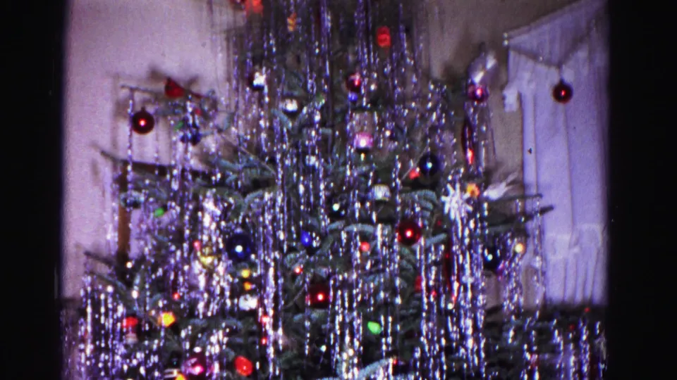 Christmas tree covered in silver icicle tinsel and multicolor glass ornaments, white curtain and window edge visible behind, 8mm home movie, Hagerstown Maryland, 1962.