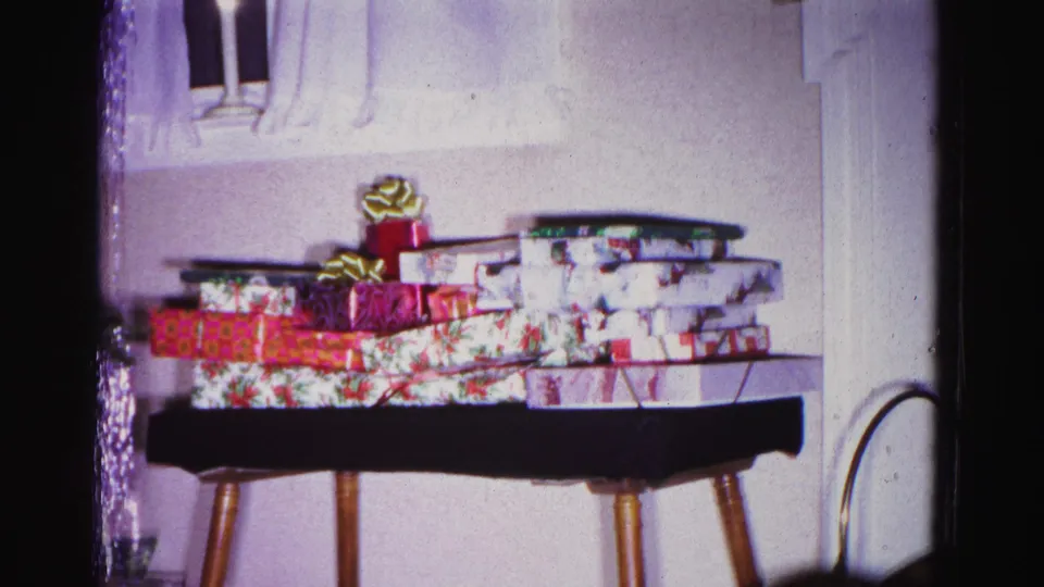 Wrapped Christmas gifts in floral and red patterned paper on a mid-century side table; from a 1962 home movie in Hagerstown, Maryland.