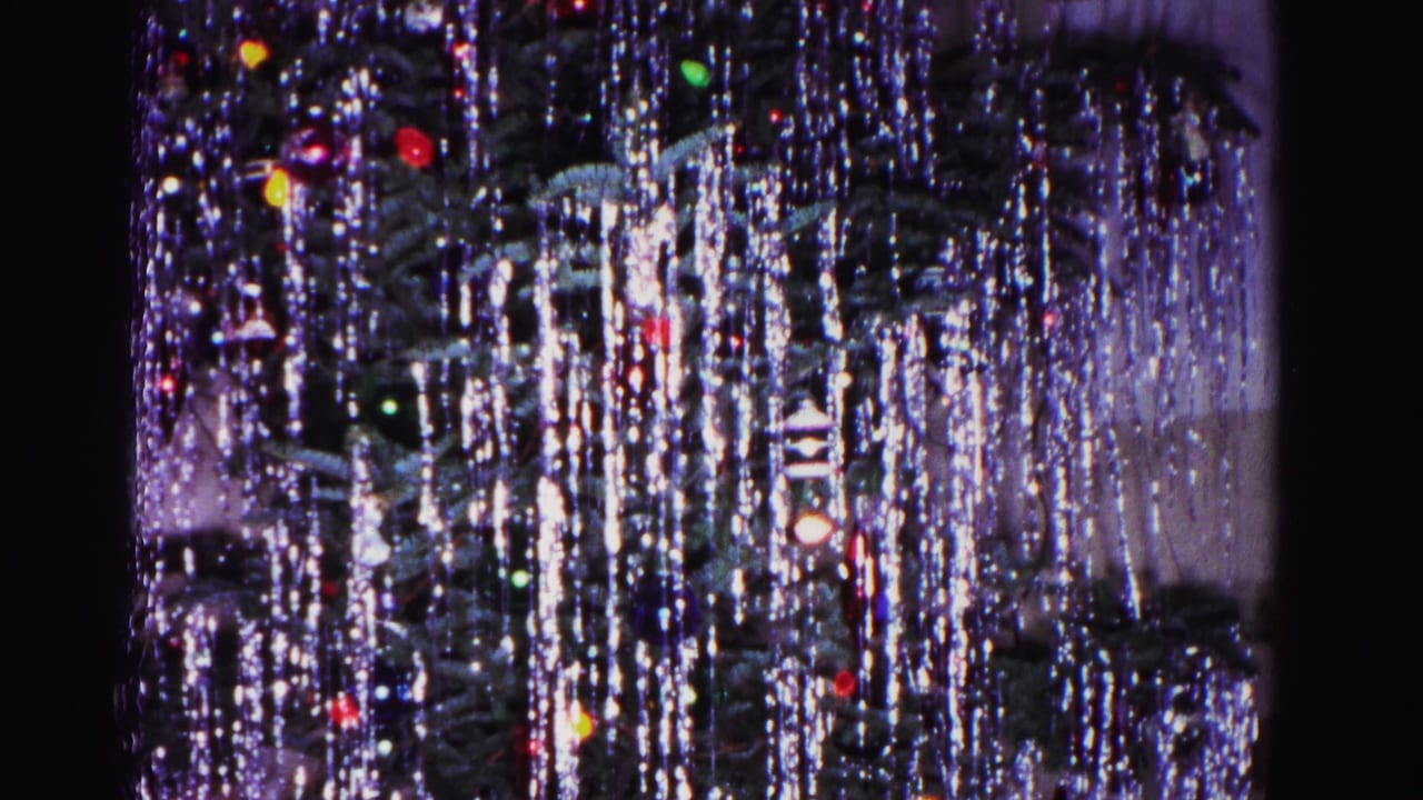 Christmas tree densely draped in silver tinsel with multicolored round ornaments, interior setting.