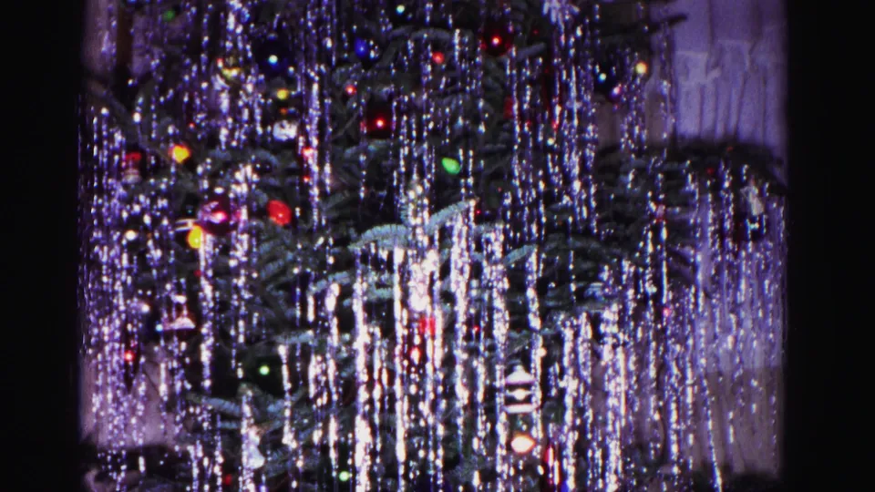 Wide view of silver-tinseled Christmas tree with multicolored bulbs, from a 1962 8mm home movie in Hagerstown, Maryland.
