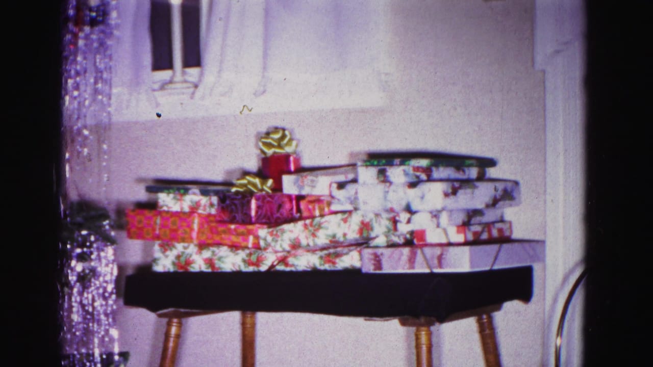 8mm frame, circa 1962, of a wooden side table bearing stacked wrapped Christmas gifts; silver tinsel from the adjacent tree frames the upper portion of the shot.