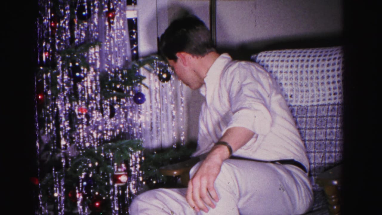Man in white shirt leans toward Christmas tree, face partially visible in profile, surrounded by dense cascading silver tinsel.