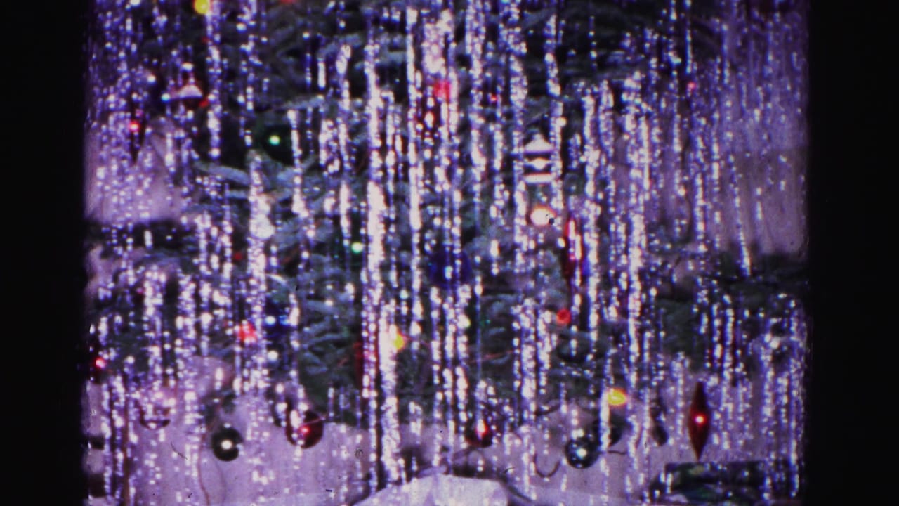 Dense silver tinsel and colorful ball ornaments dominate this close frame of a Christmas tree from an apparent 1962 home movie, with the man partially visible at the left edge.