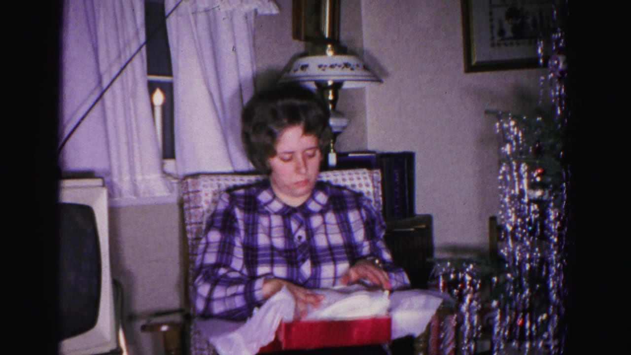 Young woman in plaid shirt unwrapping a red gift box, circa 1962, Hagerstown Maryland; silver tinsel Christmas tree and CRT television visible in background.