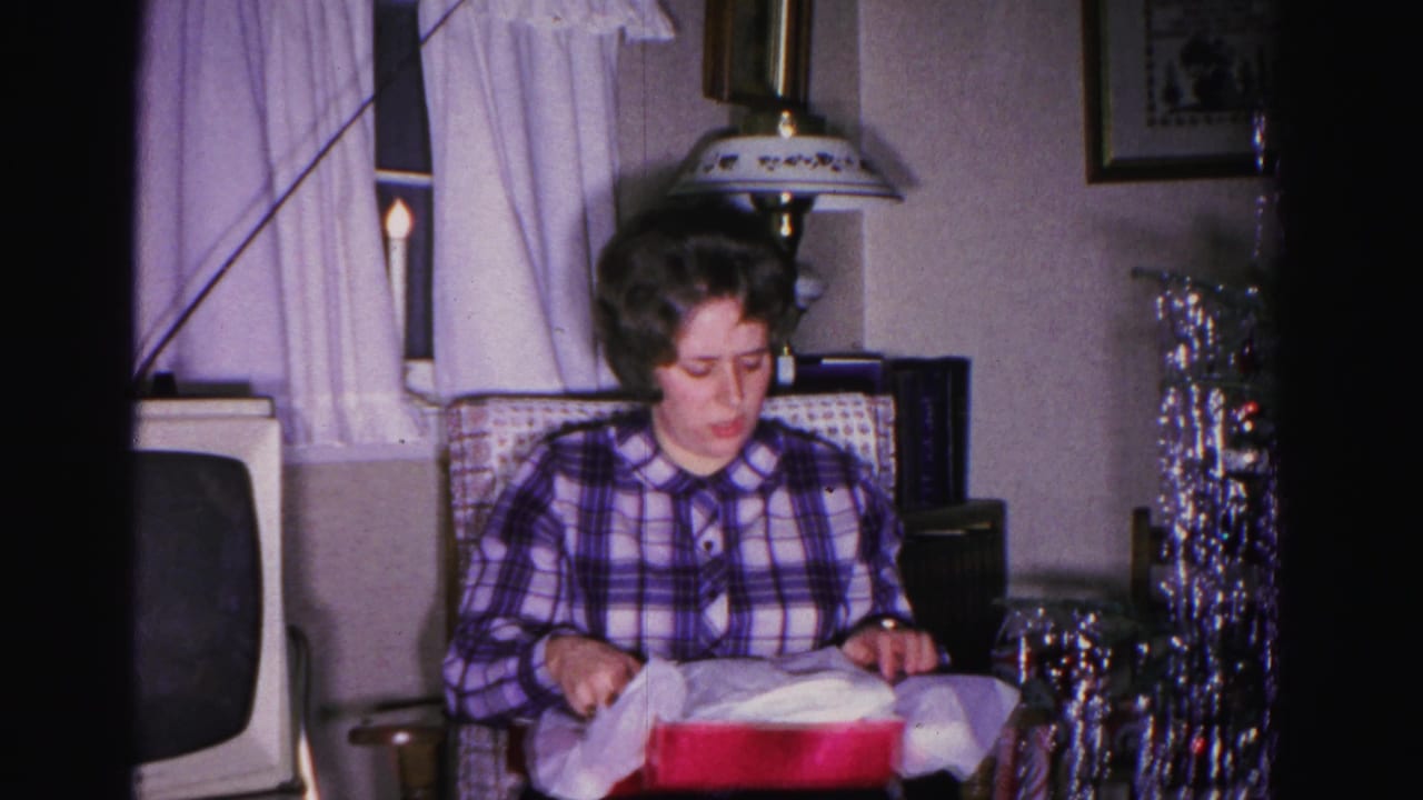 Same woman in plaid shirt seated with red gift box, tinsel Christmas tree and vintage television visible behind her.